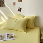 Ensemble de coussins et de draps de lit de couleur jaune pâle dans une pièce décorée avec des photos accrochées au mur.