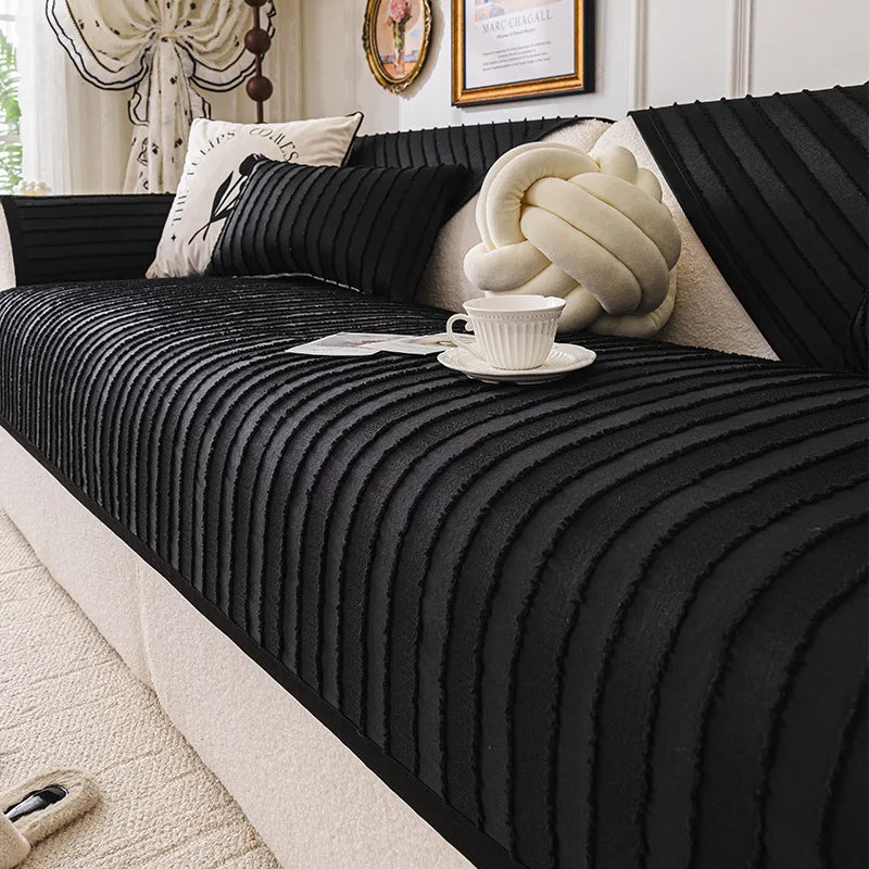 L'image montre un lit douillet avec un couvre-lit noir orné de coussins et d'un accessoire moelleux de forme noueuse, un décor élégant qui semble inviter à la détente.