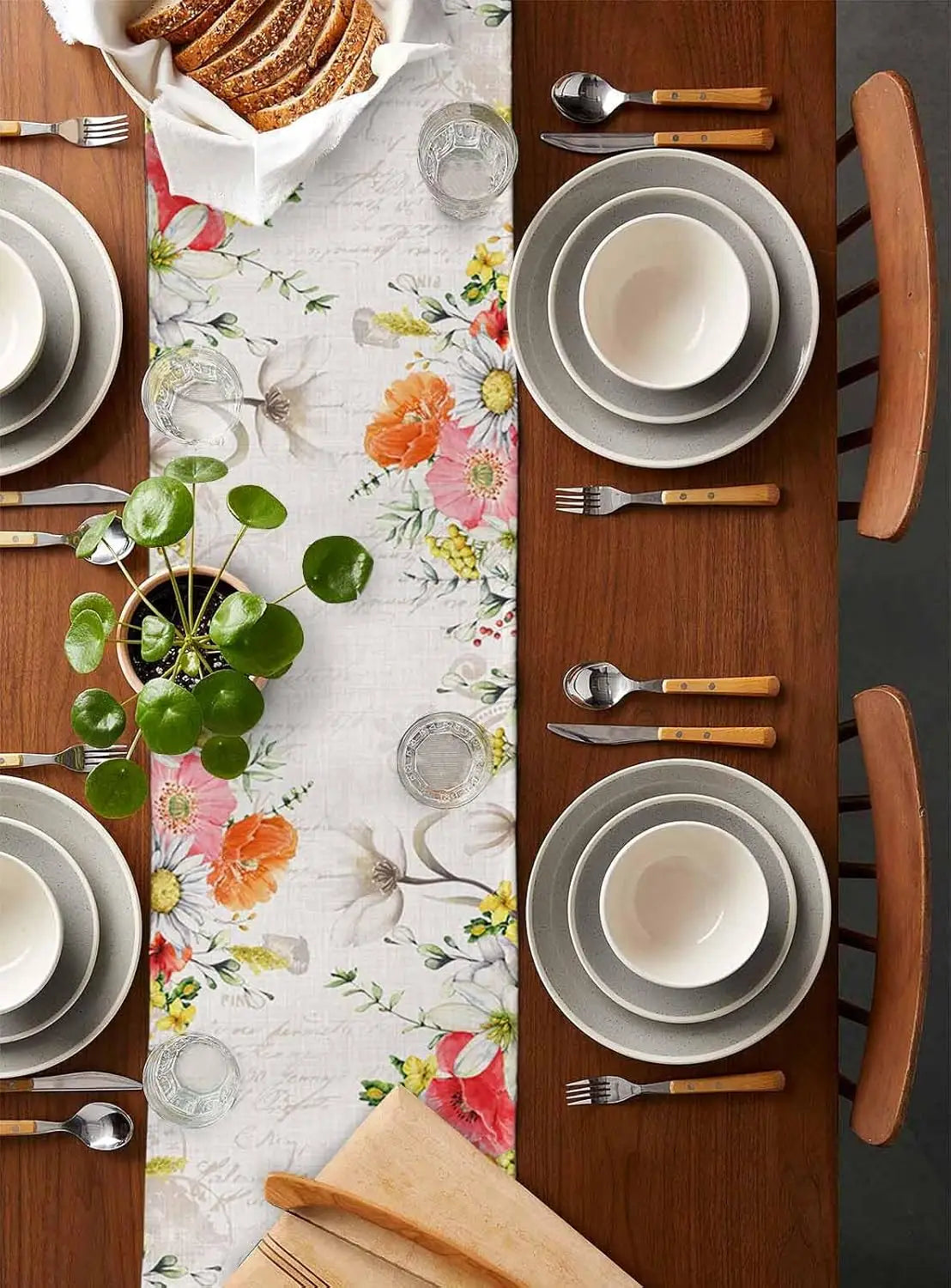 Une table dressée de façon élégante avec des assiettes et couverts en bois, un magnifique chemin de table fleuri et des plantes grasses, créant une atmosphère chaleureuse et invitante.