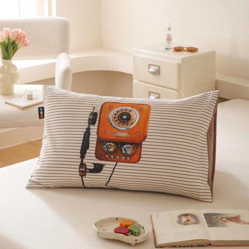 Un coussin décoratif rayé avec un vieux téléphone vintage orange, posé sur un lit dans une pièce lumineuse et élégante.