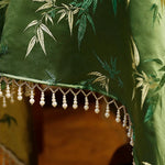 Des motifs de feuilles de bambou ornent avec élégance ce tissu vert foncé, rehaussé d'une frange de perles qui confère une touche sophistiquée à cette pièce.