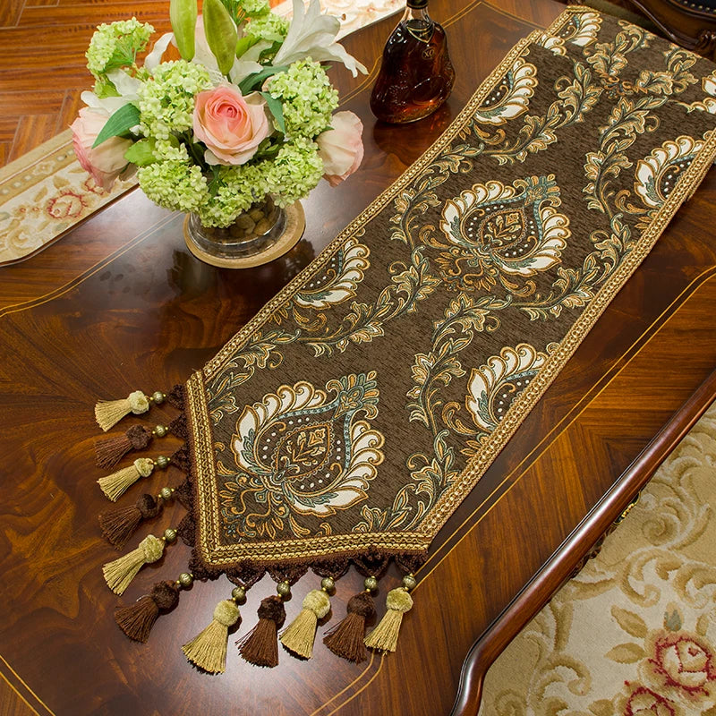 Magnifique chemin de table de couleur sombre, orné de motifs floraux dorés, assorti à un bouquet de fleurs multicolores posé sur une commode en bois.