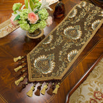 Magnifique chemin de table de couleur sombre, orné de motifs floraux dorés, assorti à un bouquet de fleurs multicolores posé sur une commode en bois.