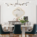 Salle à manger élégante avec un grand lustre moderne à plusieurs branches, un miroir décoratif encadré sur le mur, une table en marbre avec des chaises rembourrées en velours bleu, des fleurs dans un vase, et des décorations murales, créant une atmosphère chaleureuse et sophistiquée.