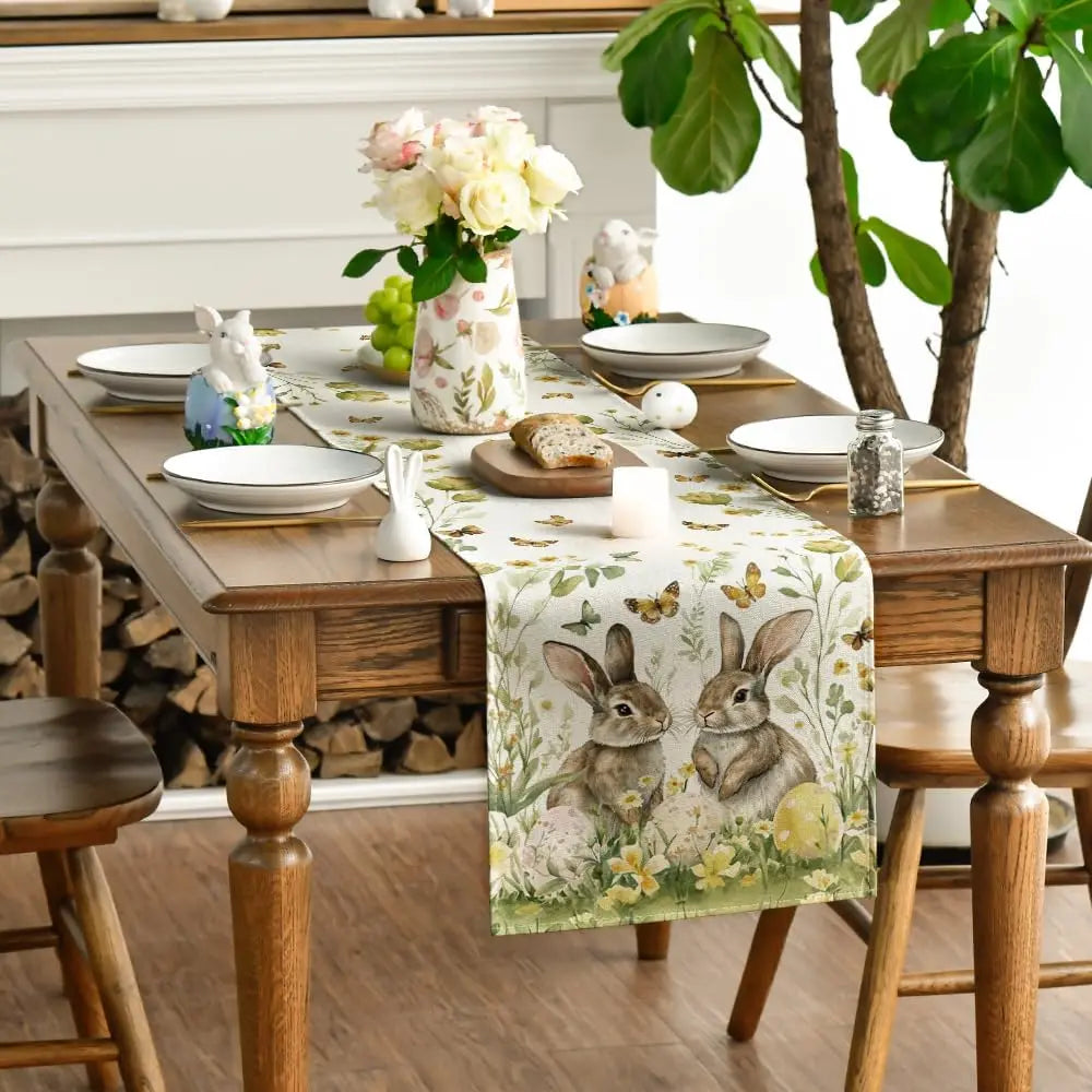 Une table à manger rustique avec une nappe ornée de lapins et de fleurs, décorée de bougies et de figurines de Pâques, créant une ambiance chaleureuse et printanière.
