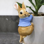 Lapin doré mignon avec un bandana bleu autour du cou, posé près d'une plante en pot.