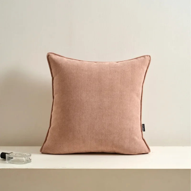 Coussin décoratif rose poudreux en lin posé sur une étagère blanche avec un vase en verre.