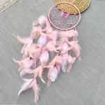 Un capteur de rêves rose décoré de plumes légères et d'une toile d'araignée ajoute une touche de douceur et de féminité à cette scène apaisante.