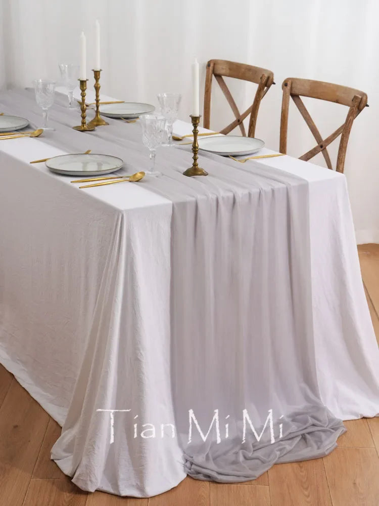 Table dressée pour un repas avec des verres, des plats, des chandeliers dorés et des chaises en bois sur un sol en bois.