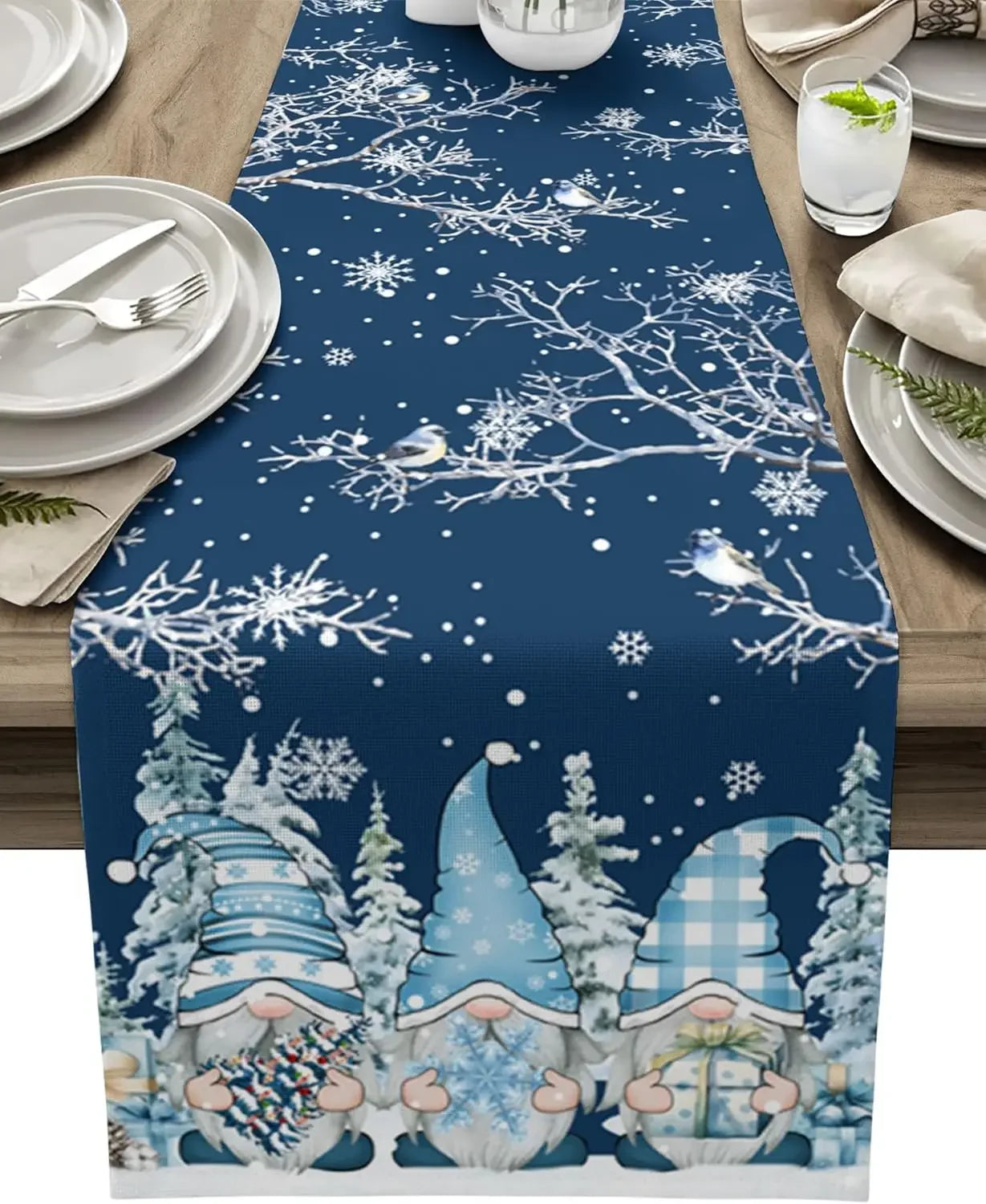 Une table de Noël décorée avec une nappe imprimée de motifs de flocons de neige, de sapins et de gnomes mignons dans un paysage enneigé.