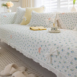 Cette image montre un lit douillet avec de jolis coussins et une couverture blanche à fleurs, créant une ambiance chaleureuse et accueillante dans une chambre élégante.