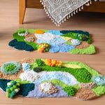 Tapis décoratif en fibre naturelle représentant un paysage coloré avec des fleurs, des rochers et des cours d'eau stylisés.