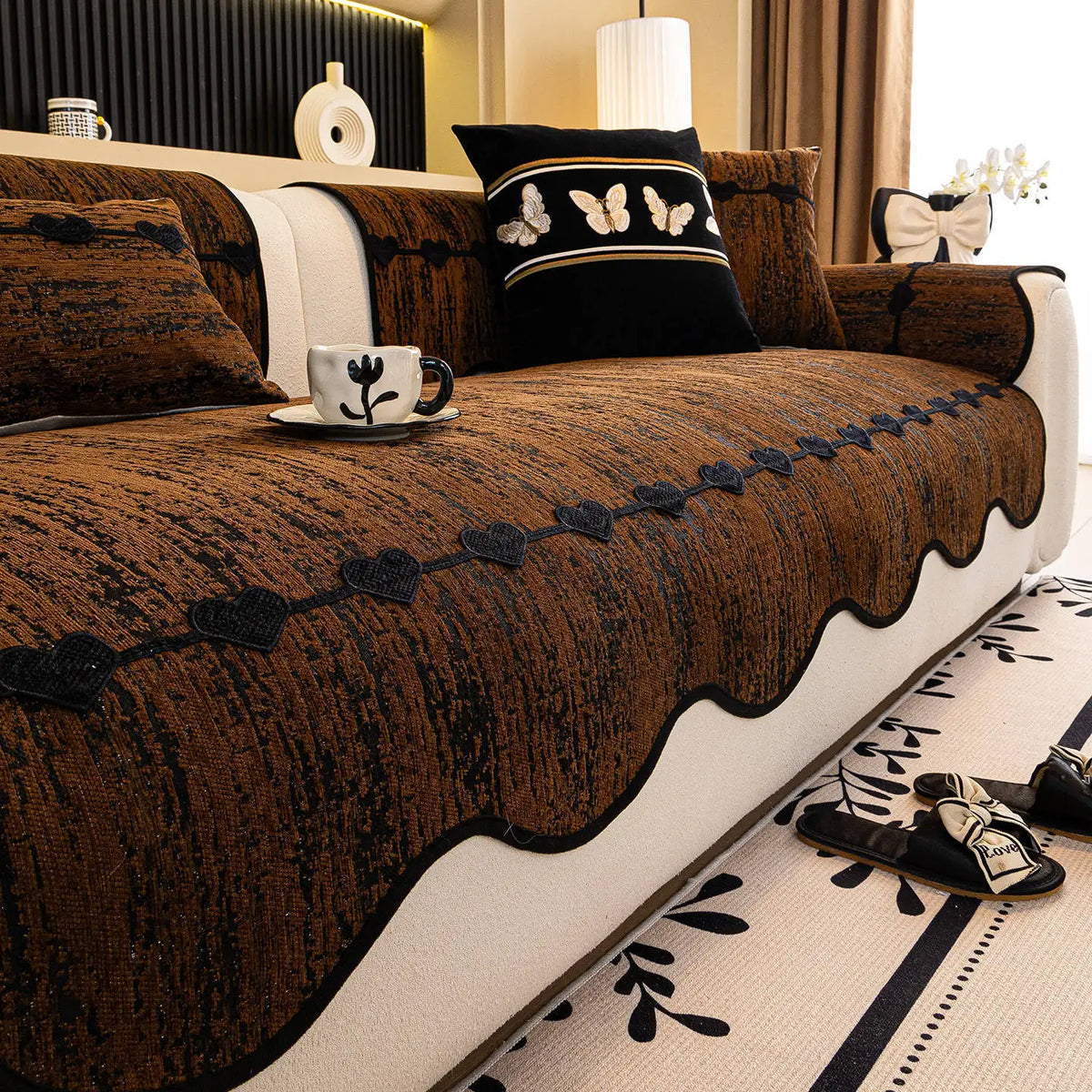 Salon élégant avec un canapé brun en velours orné de motifs de papillons et de fleurs, accompagné d'accessoires décoratifs noirs et blancs pour créer une atmosphère chaleureuse et raffinée.