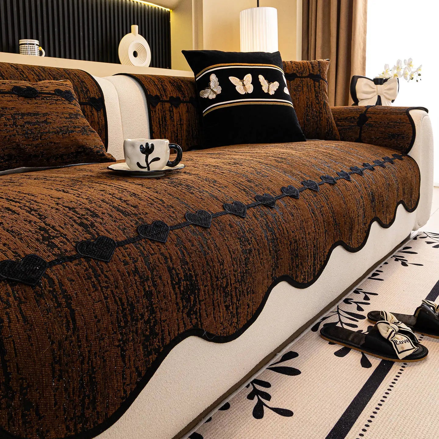 Salon élégant avec un canapé brun en velours orné de motifs de papillons et de fleurs, accompagné d'accessoires décoratifs noirs et blancs pour créer une atmosphère chaleureuse et raffinée.