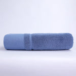 Une serviette de bain bleue en tissu éponge de grande taille, plié sur un fond blanc.