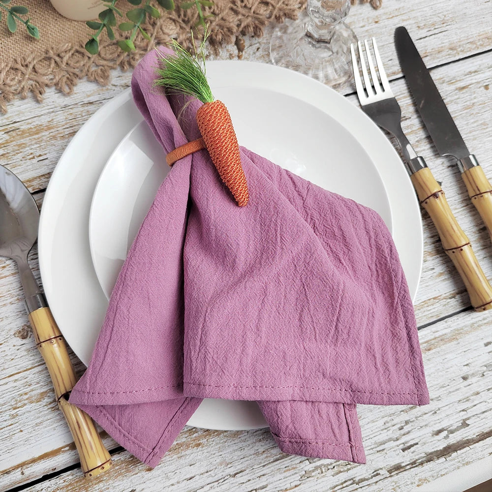 Une serviette de table violette nouée d'un ruban orange est posée sur une assiette blanche, avec des ustensiles de cuisine en bambou.
