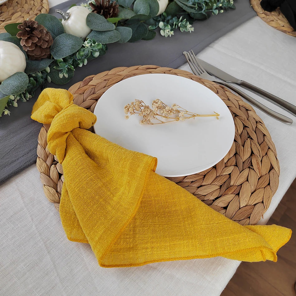 Une assiette blanche posée sur un napperon tressé, entourée de décorations végétales automnales, avec un beau linge de table jaune.