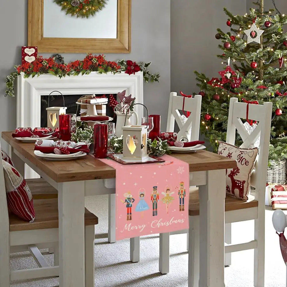 Cette image présente une table de salle à manger joliment décorée pour Noël, avec des ornements rouges et verts, des bougies, et un arbre de Noël dans un coin. La table est recouverte d'un chemin de table avec des motifs de personnages de Noël et l'inscription "Joyeux Noël".