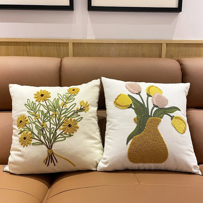 Deux coussins décoratifs blancs avec des motifs de fleurs jaunes et vertes placés sur un canapé beige.