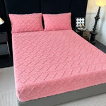 Un élégant ensemble de literie rose composé d'un couvre-lit matelassé et de deux oreillers assortis, créant une ambiance chaleureuse et accueillante dans la chambre.