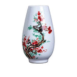 Un vase élégant décoré de fleurs de cerisier rouges et de bambous verts sur un fond blanc.