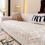 Un beau canapé confortable avec des motifs graphiques beiges et blancs, décoré de coussins et d'un ours en peluche, dans un décor chaleureux et élégant.