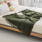Couverture en laine verte avec des franges déposée sur un lit blanc, créant une ambiance douillette et confortable dans la chambre.