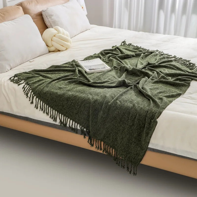 Couverture en laine verte avec des franges déposée sur un lit blanc, créant une ambiance douillette et confortable dans la chambre.