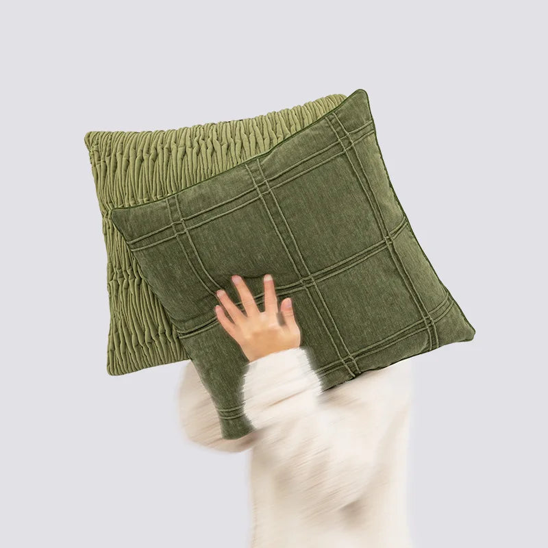 Coussin décoratif vert olive avec un motif quadrillé et une texture plissée, retenu par une main blanche en gros plan.