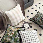 Cette image démontre une décoration de chambre élégante et moderne, avec des coussins aux motifs géométriques et floraux, ainsi qu'une couverture et un tapis texturés.