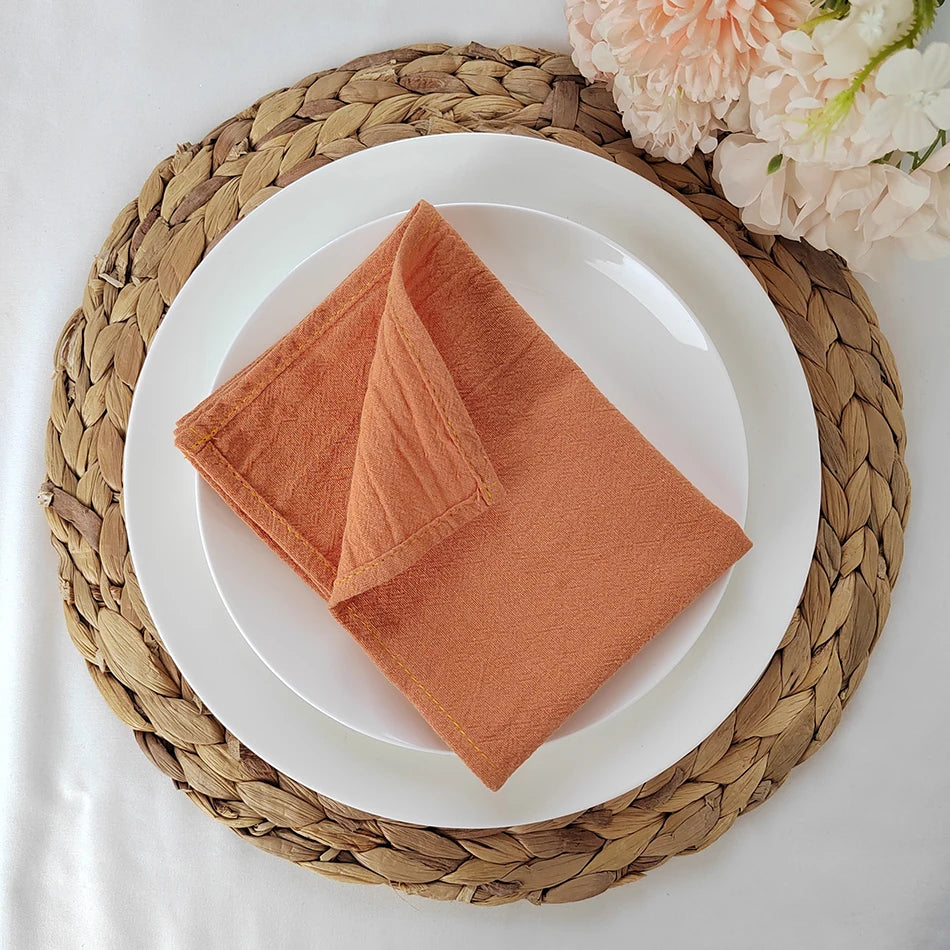 Un élégant linge de table se compose d'une serviette en coton doux de couleur terre cuite, posée sur une assiette blanche sur un joli set de table en vannerie.