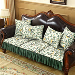 Canapé vintage tapissé de motifs floraux sur fond vert, avec des coussins assortis posés sur un canapé en cuir sombre à l'intérieur d'un salon élégant.