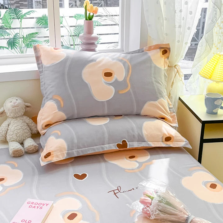 Couette et taies d'oreiller avec motif de fleurs et de formes abstraites dans des tons de gris et de orange pâle, placés sur un lit avec un éclairage naturel et des accents de décoration.