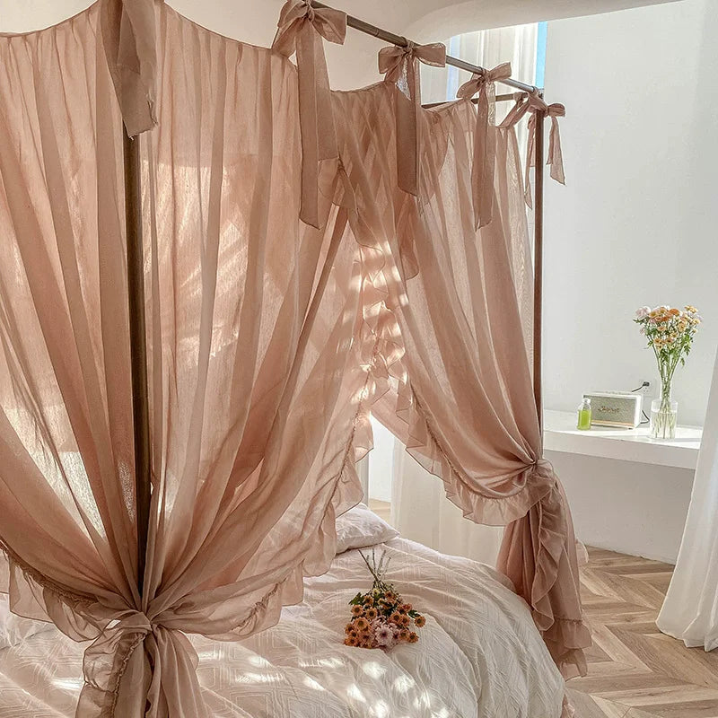 L'image montre un lit à baldaquin aux rideaux beige clair, avec un petit bouquet de fleurs posé sur le lit. La pièce semble accueillante et lumineuse.