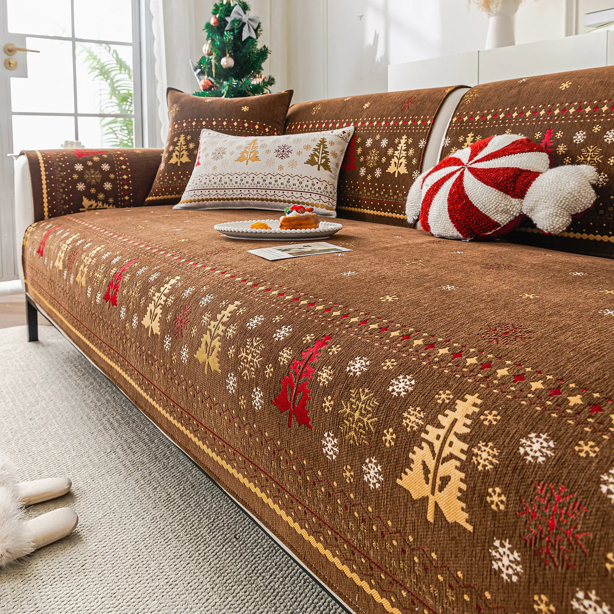 Une décoration de Noël chaleureuse avec un canapé confortable recouvert d'un plaid brodé de motifs hivernaux.