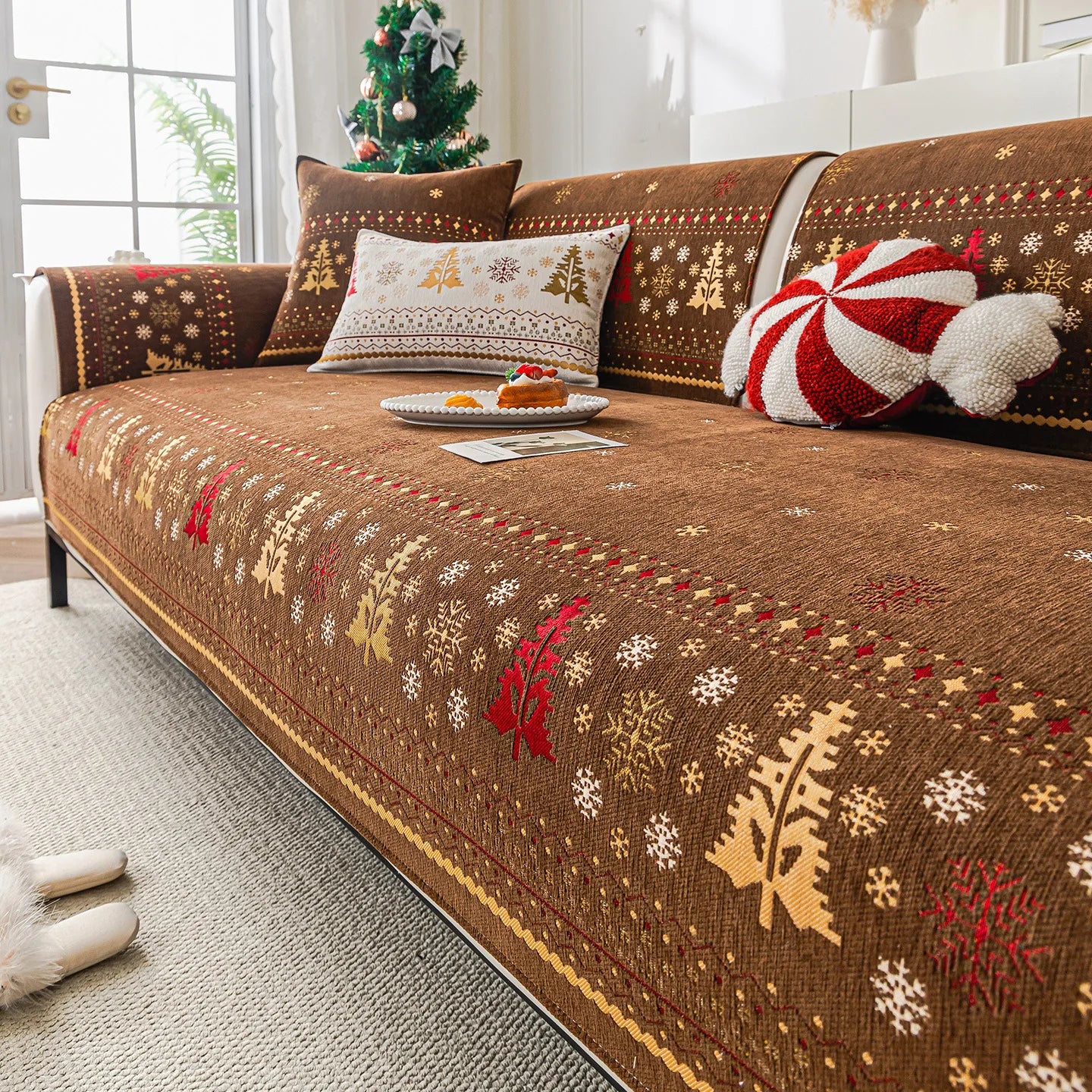 Une décoration de Noël chaleureuse avec un canapé confortable recouvert d'un plaid brodé de motifs hivernaux.