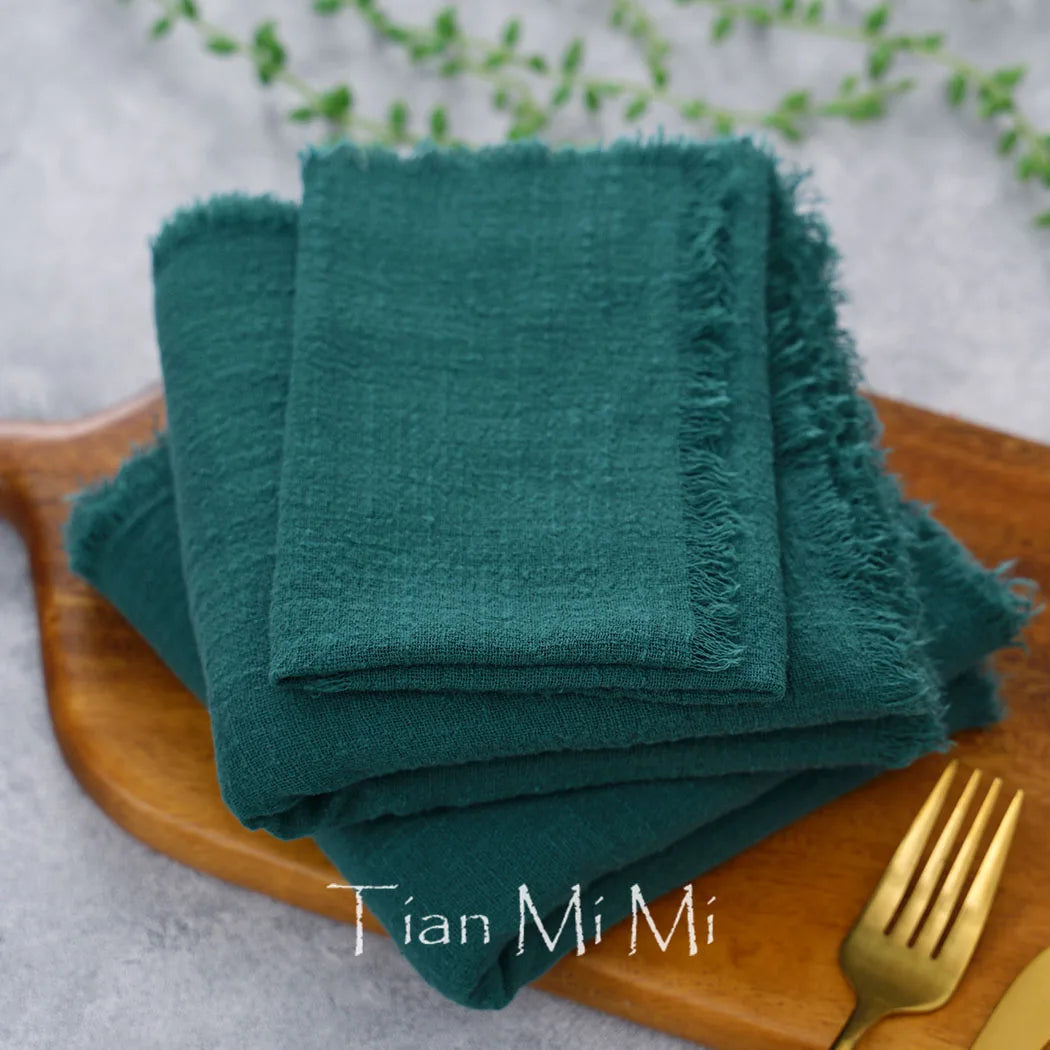 Serviettes de table en coton vert foncé sur un plateau en bois, avec des couverts métalliques à proximité.