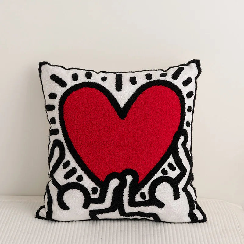 Un coussin orné d'un grand cœur rouge, entouré de motifs graphiques en noir et blanc.