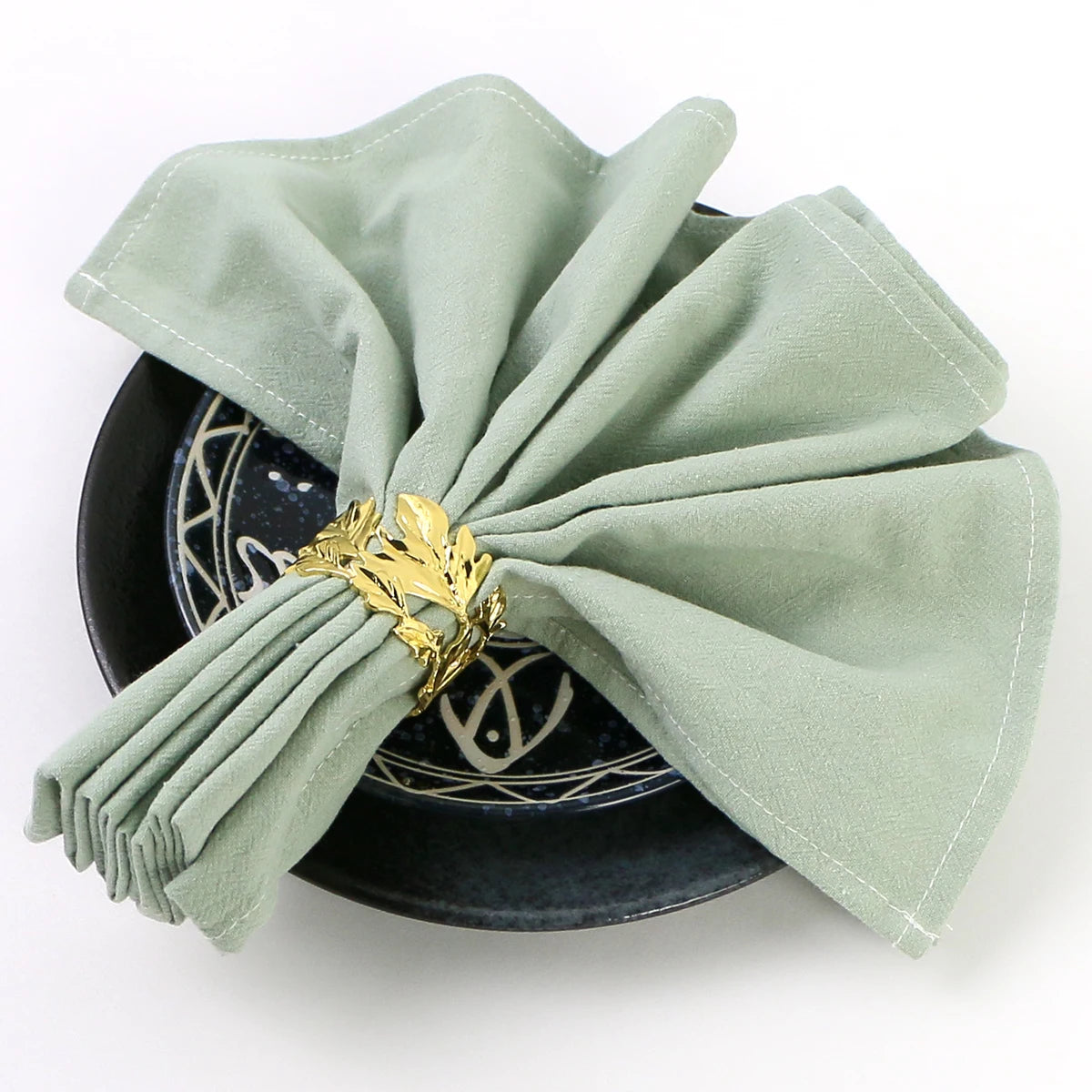 Élégante vaisselle noire et dorée avec des serviettes en soie vert menthe soigneusement pliées, créant une présentation raffinée et esthétique.