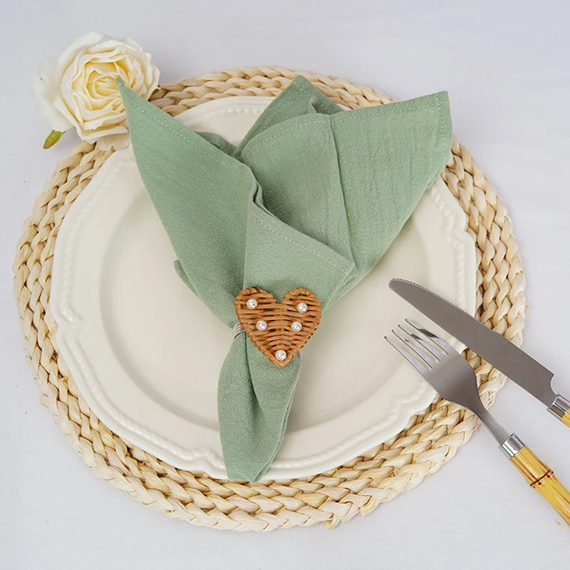 Une élégante table de dîner avec une serviette verte pliée de manière artistique, ornée d'un coeur en osier tressé et d'une rose blanche, posée sur un joli set de table en osier.
