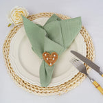 Une élégante table de dîner avec une serviette verte pliée de manière artistique, ornée d'un coeur en osier tressé et d'une rose blanche, posée sur un joli set de table en osier.
