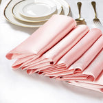 Une pile de serviettes de table en satin rose, disposées avec élégance auprès d'assiettes et de couverts dorés, créant une mise en place raffinée.