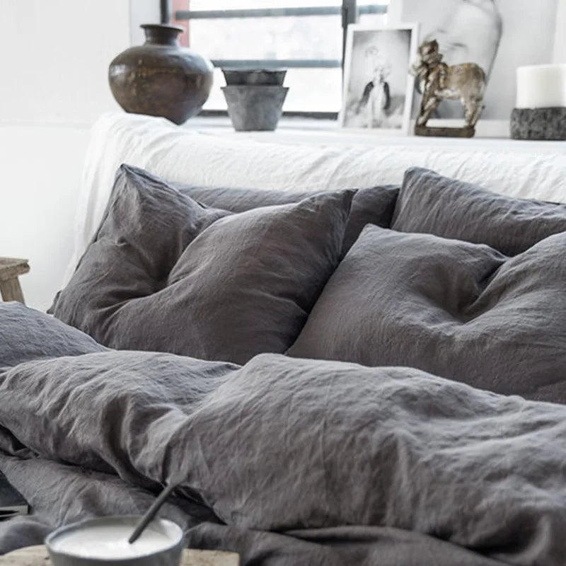 Cette image présente un lit douillet recouvert de draps et de coussins gris, créant une atmosphère apaisante et cocooning dans la pièce, avec des éléments décoratifs comme des vases et des statues disposés sur une étagère.