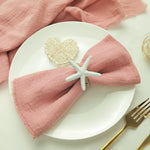 Une décoration de table élégante avec une serviette rose pâle et un élément décoratif en forme d'étoile de mer sur une assiette blanche.