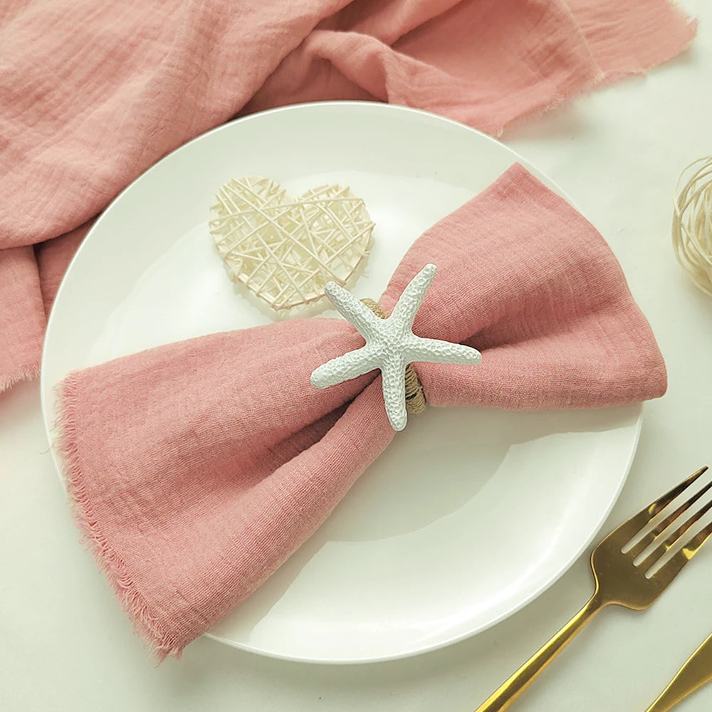 Une décoration de table élégante avec une serviette rose pâle et un élément décoratif en forme d'étoile de mer sur une assiette blanche.