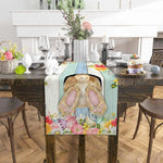 Table élégamment décorée pour Pâques, avec un chemin de table fleuri, des fleurs, des lapins en céramique et d'autres éléments de décoration festive.