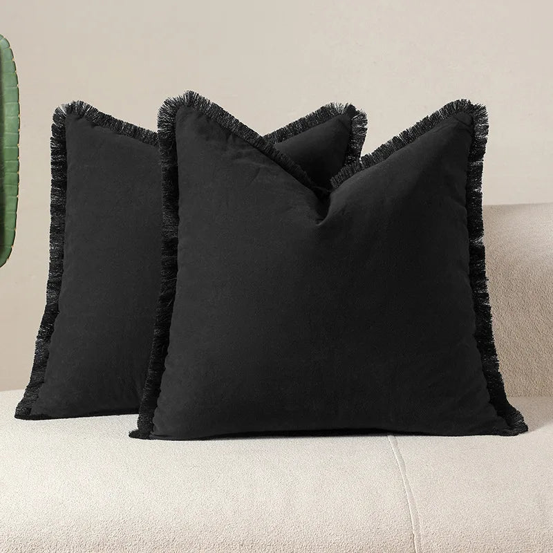 Coussins décoratifs noirs avec des franges élégantes, posés sur un canapé beige, créant une ambiance douce et chaleureuse dans la pièce.