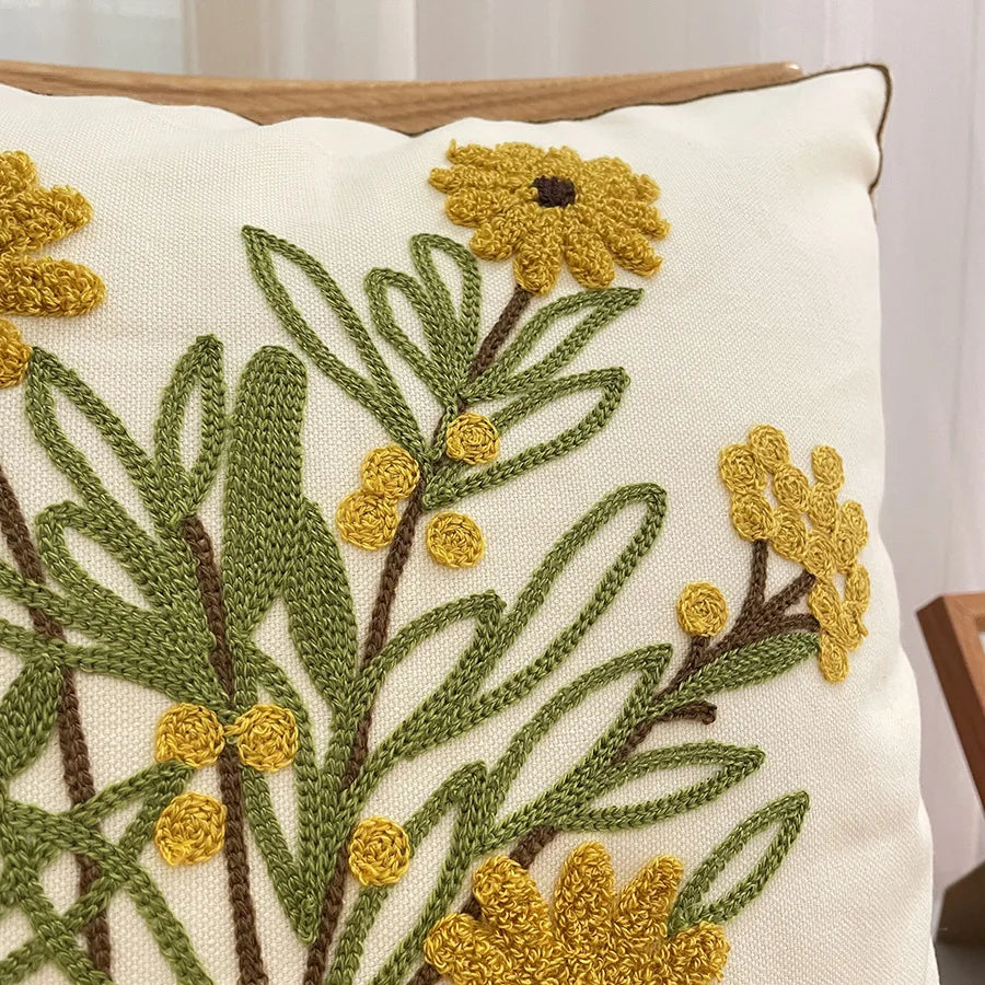 Coussin décoré de jolies fleurs jaunes et vertes brodées avec soin sur un fond blanc.