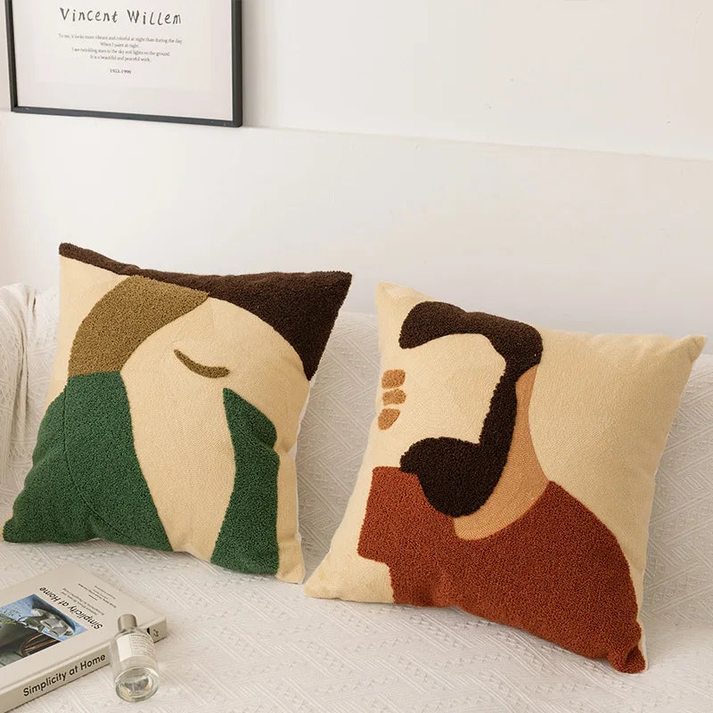 Deux coussins décoratifs colorés avec des motifs abstraits et géométriques, placés devant un cadre mural avec un texte.