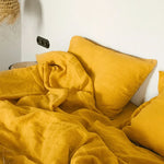 Coussin jaune vif plissé et froissé, placé sur un lit blanc.